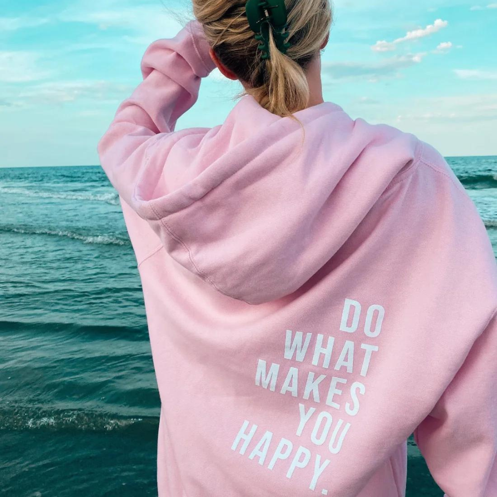 Sofia Oversized Kapuzenpullover in Hellrosa mit weissem Schriftzug-Print am Strand