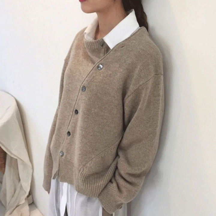 Solveig asymmetrischer Cardigan in Beige, Seitenansicht an Wand gelehnt